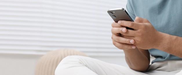 Image of Man typing message on mobile phone indoors, closeup. Banner design with space for text