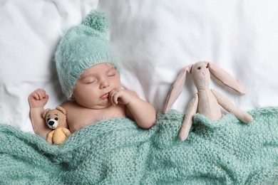 Photo of Cute little baby with toys sleeping under knitted plaid in bed, top view