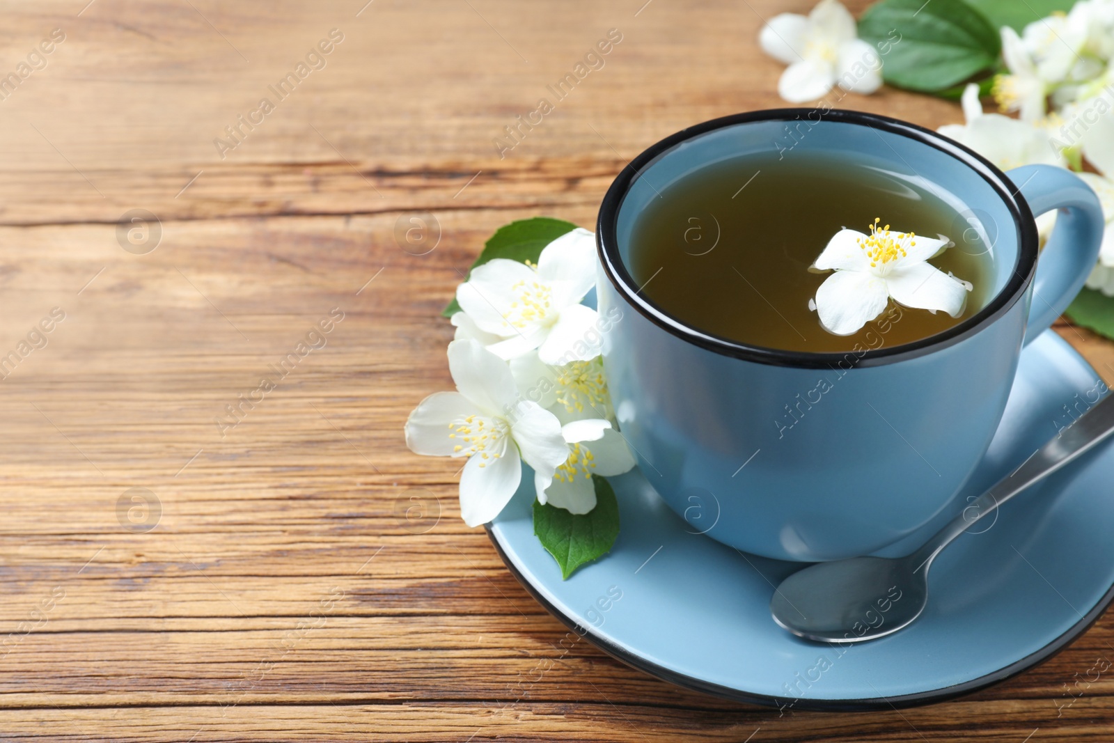 Photo of Cup of tea and fresh jasmine flowers on wooden table. Space for text