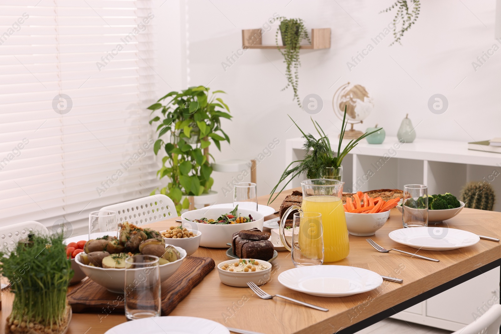 Photo of Healthy vegetarian food, jug of juice, cutlery, glasses and plates on wooden table indoors