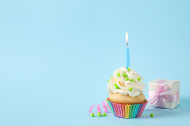 Photo of Birthday cupcake with candle and gift box on light blue background. Space for text