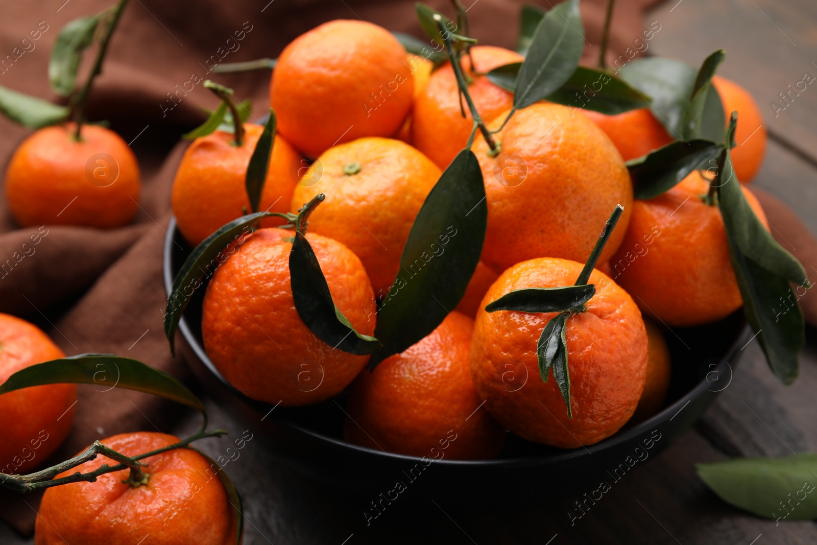 Photo of Fresh ripe tangerines with green leaves in bowl on table, closeup