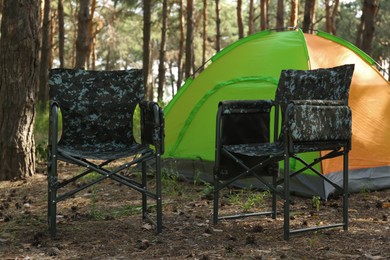 Camouflage chairs near camping tent in forest on sunny day