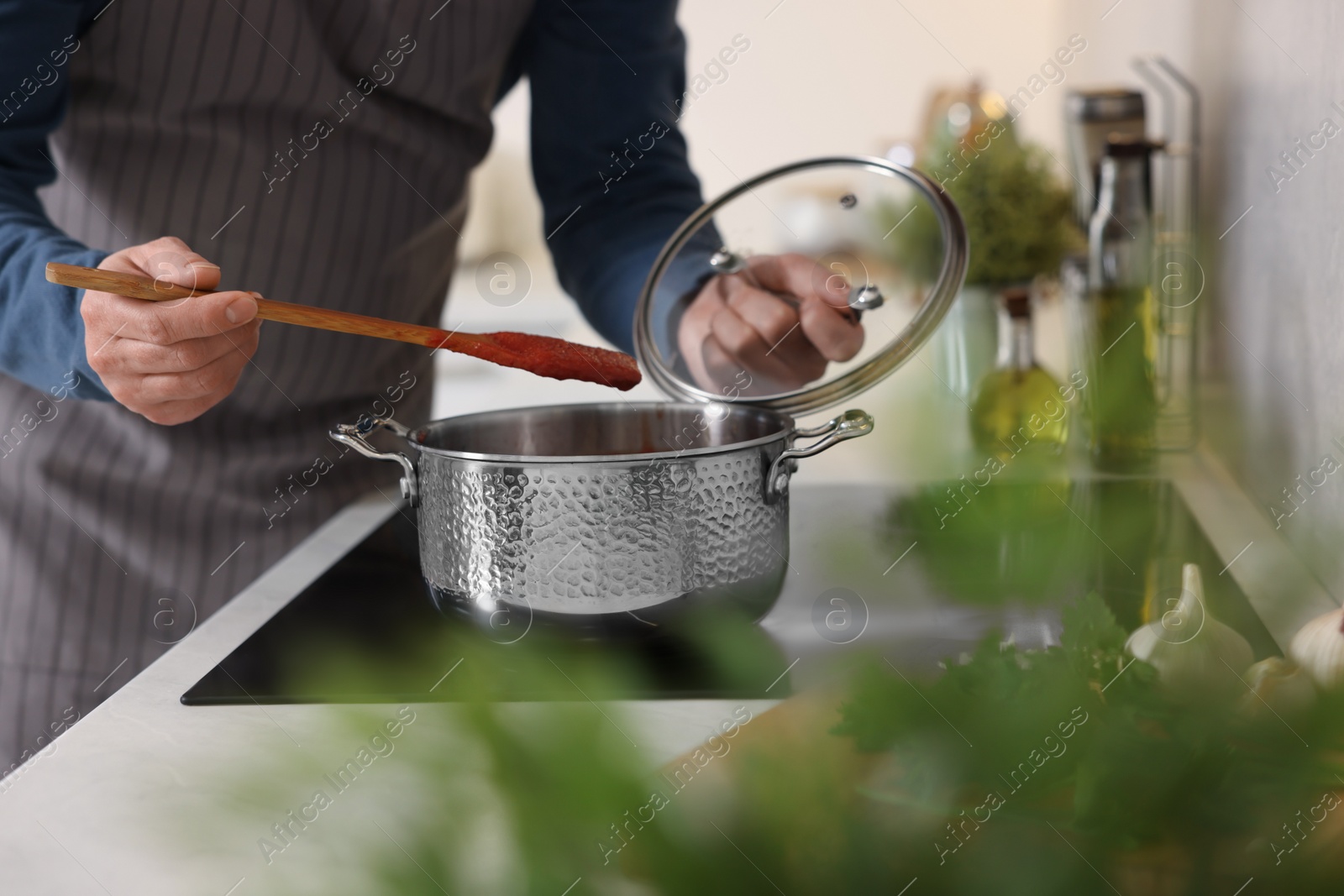 Photo of Man cooking tomato soup on cooktop in kitchen, closeup