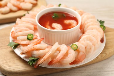 Tasty boiled shrimps with cocktail sauce, chili and parsley on light wooden table, closeup