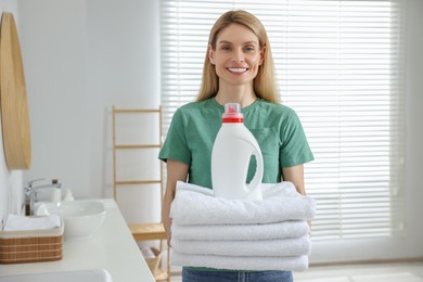 Photo of Woman holding clean towels and fabric softener in bathroom, space for text