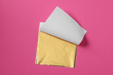 Photo of Edible gold leaf sheet on pink background, top view