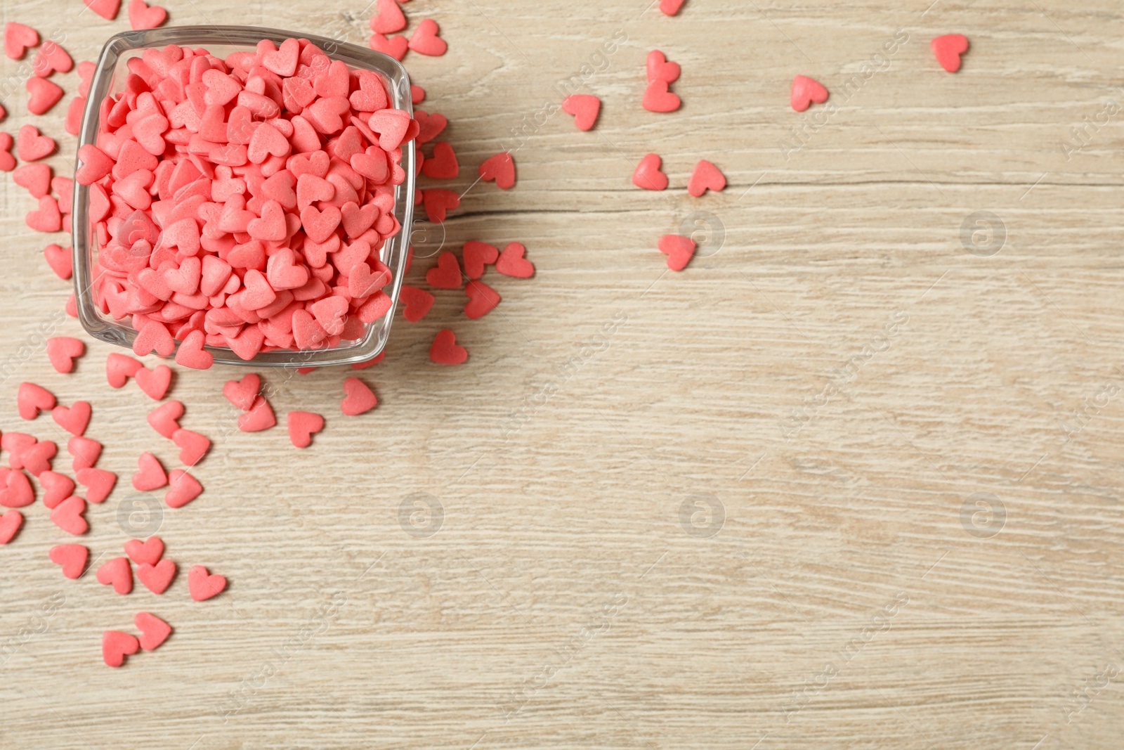 Photo of Pink heart shaped sprinkles and glass bowl on light wooden table, flat lay. Space for text