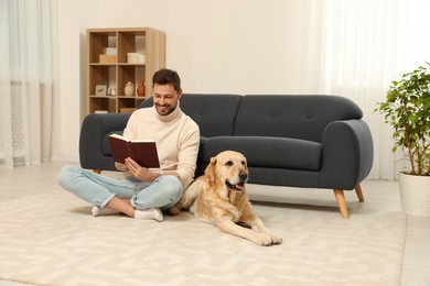 Man reading book on floor near his cute Labrador Retriever at home