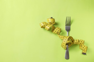 Fork and measuring tape on green background, top view with space for text. Diet concept