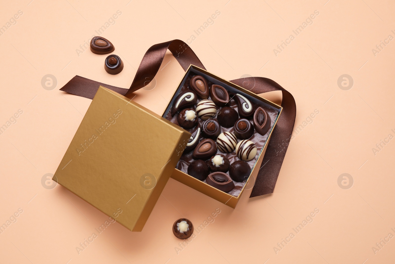 Photo of Open box of delicious chocolate candies on beige background, flat lay