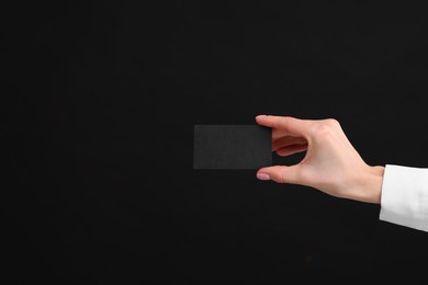 Woman holding blank business card on black background, closeup. Space for text