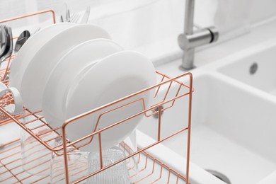 Photo of Drying rack with clean dishes near sink in kitchen, closeup