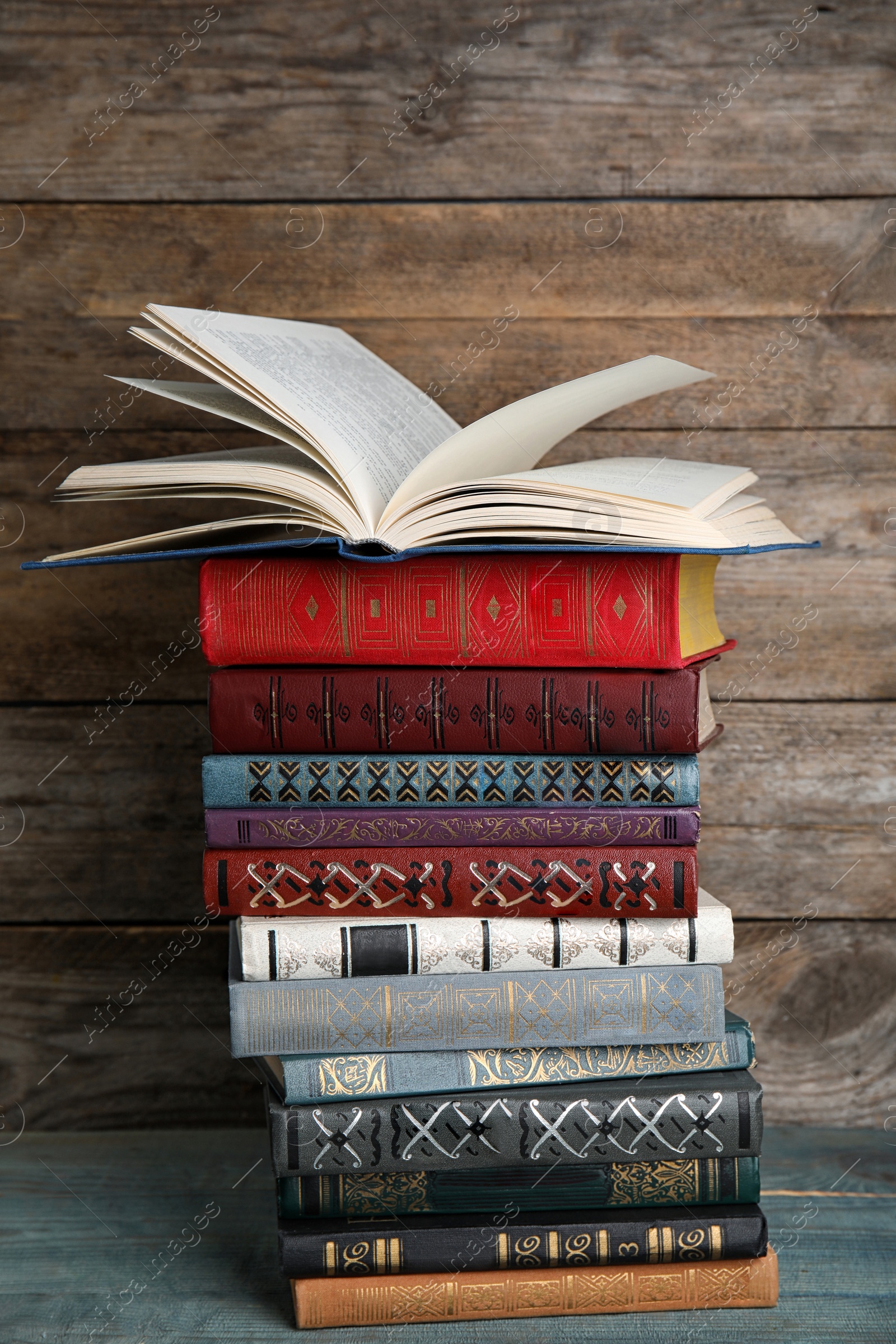 Photo of Stack of hardcover books on light blue table against wooden background