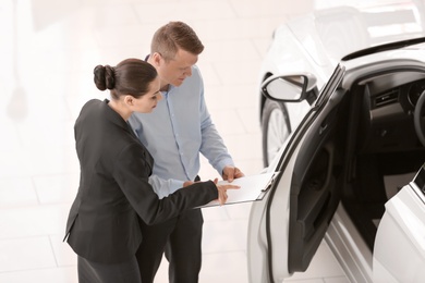 Photo of Young salesman working with client in car dealership
