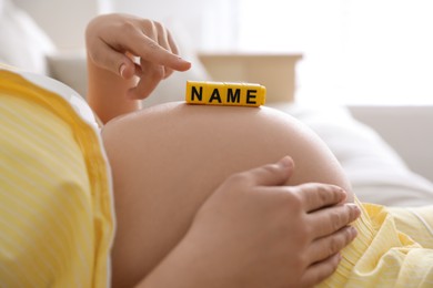 Pregnant woman with cubes on belly indoors, closeup. Choosing baby name