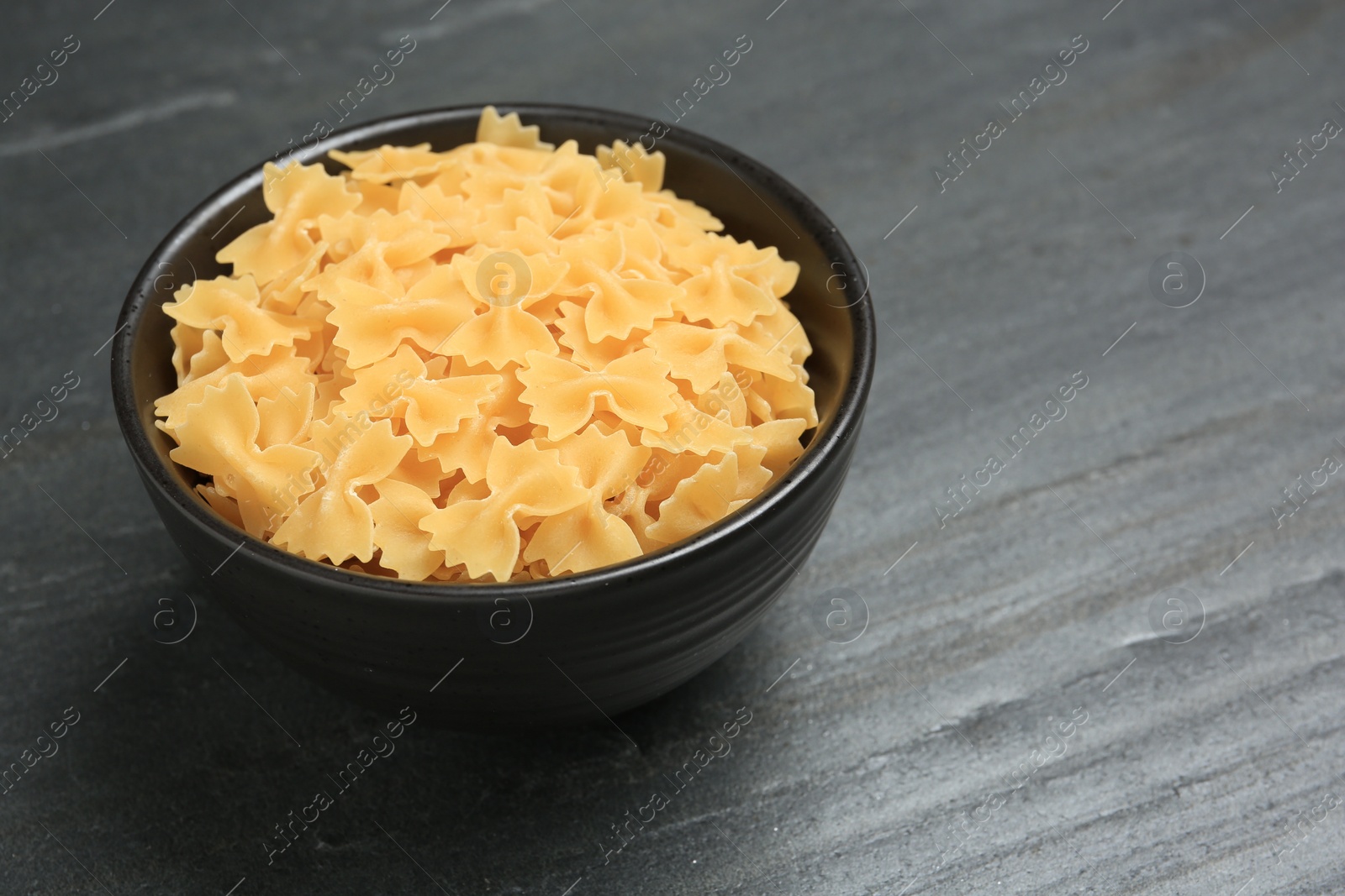 Photo of Raw farfalle pasta in bowl on grey table, closeup. Space for text