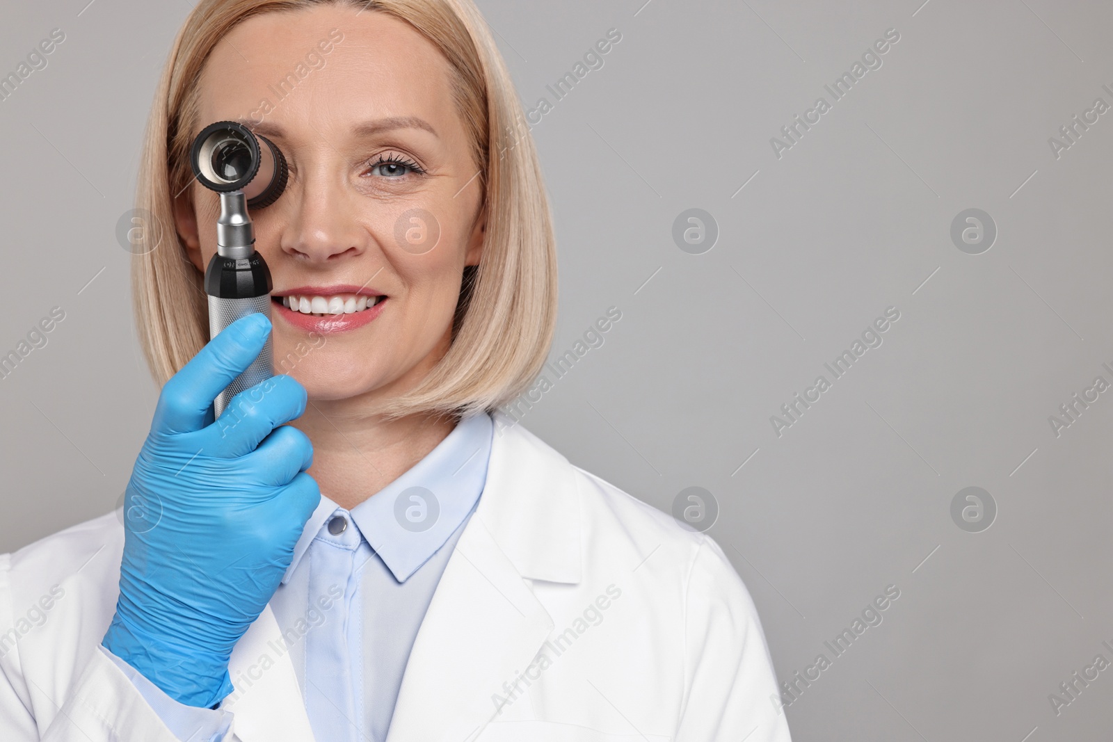 Photo of Happy dermatologist using dermatoscope on grey background. Space for text