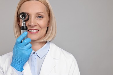Photo of Happy dermatologist using dermatoscope on grey background. Space for text