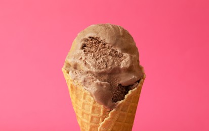 Delicious chocolate ice cream in waffle cone on pink background, closeup