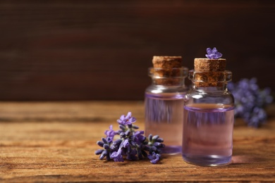 Photo of Bottles of essential oil and lavender flowers on wooden table. Space for text