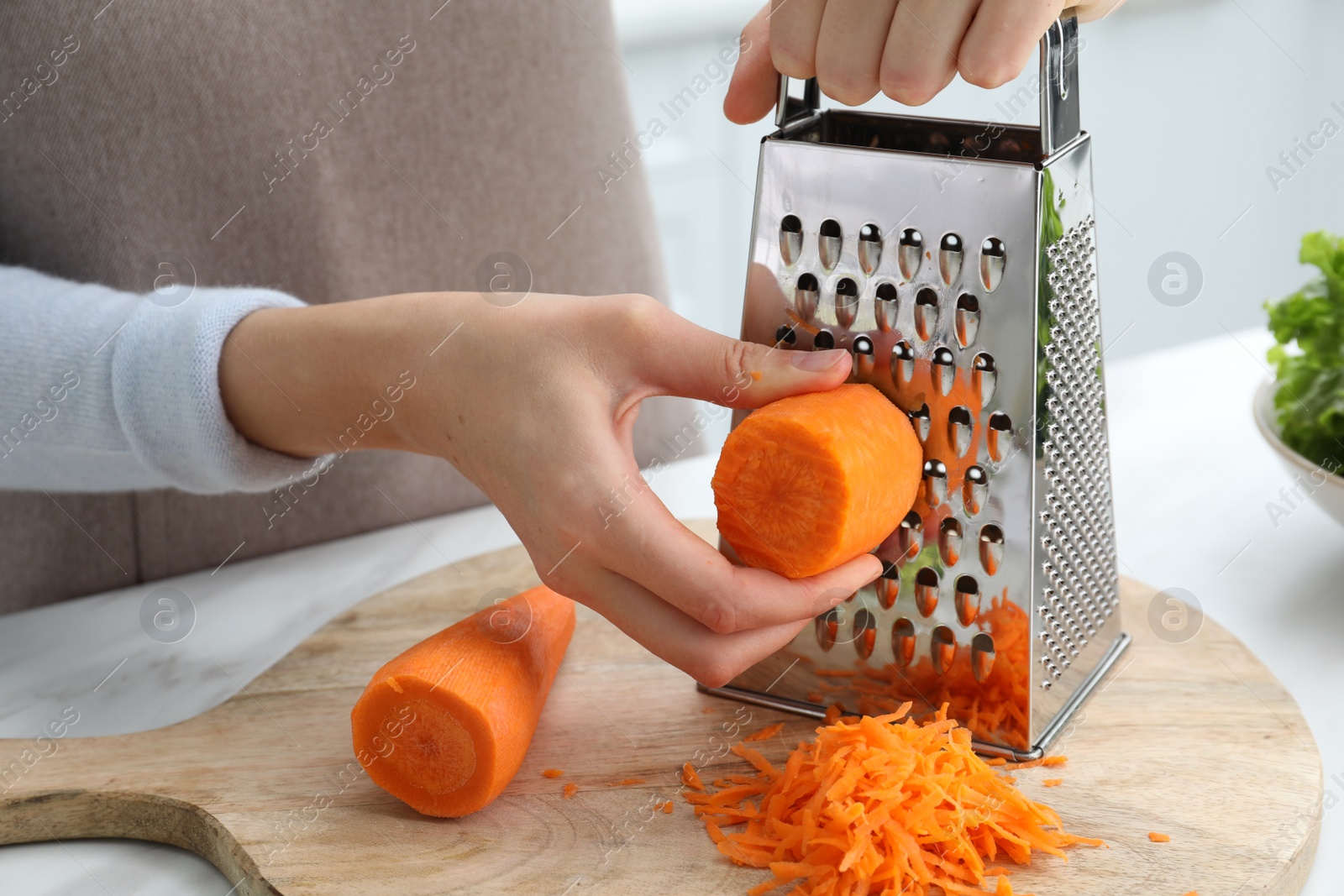 Photo of Woman grating fresh ripe carrot at kitchen table, closeup