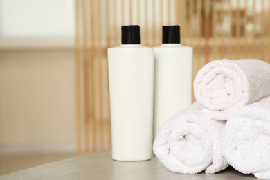 Soft folded terry towels and cosmetic bottles on light gray wooden table indoors. Space for text