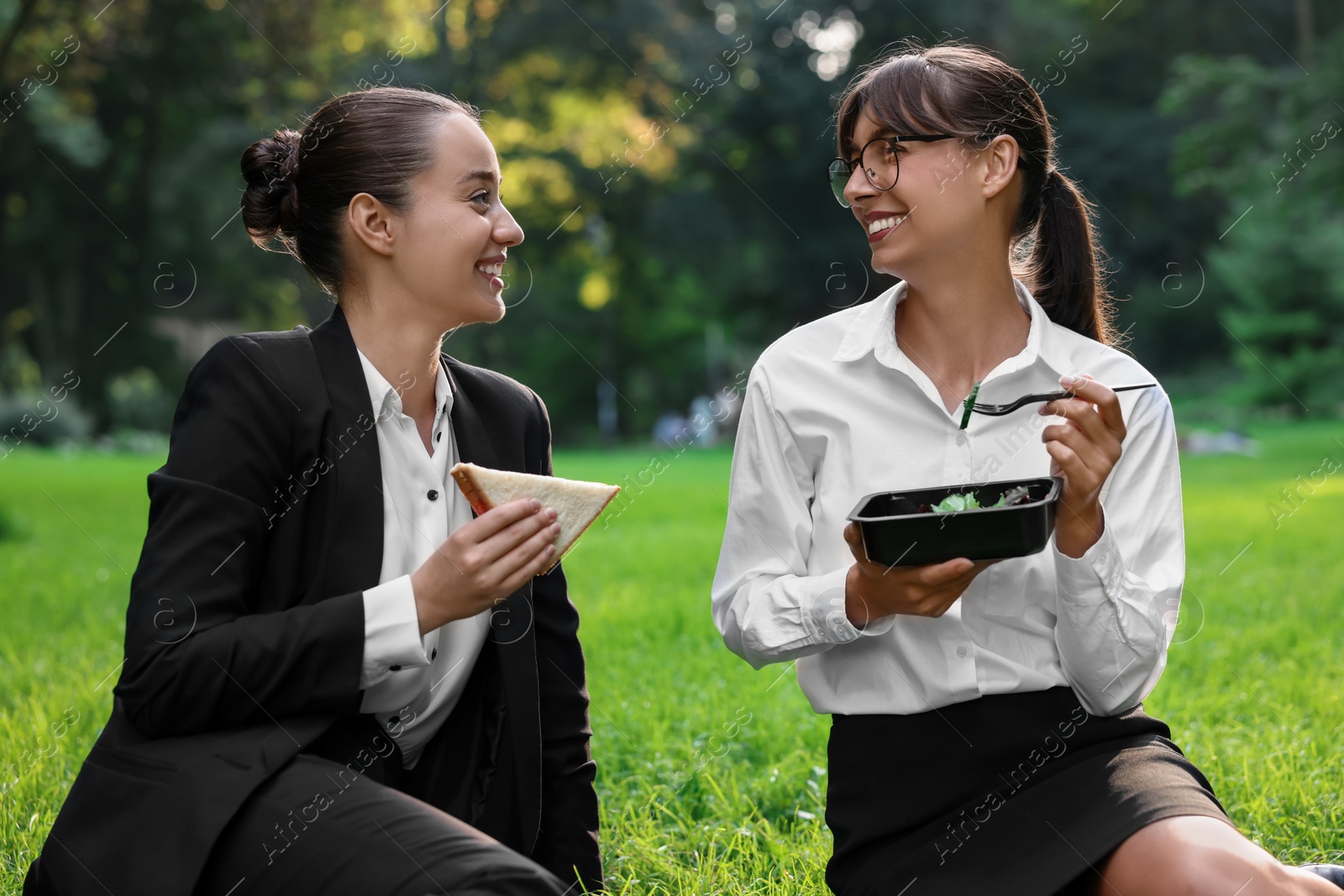 Photo of Happy colleagues having business lunch on green grass in park