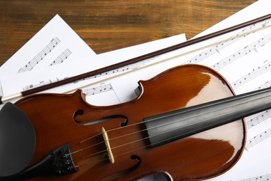 Photo of Beautiful violin, bow and note sheets on wooden table, flat lay