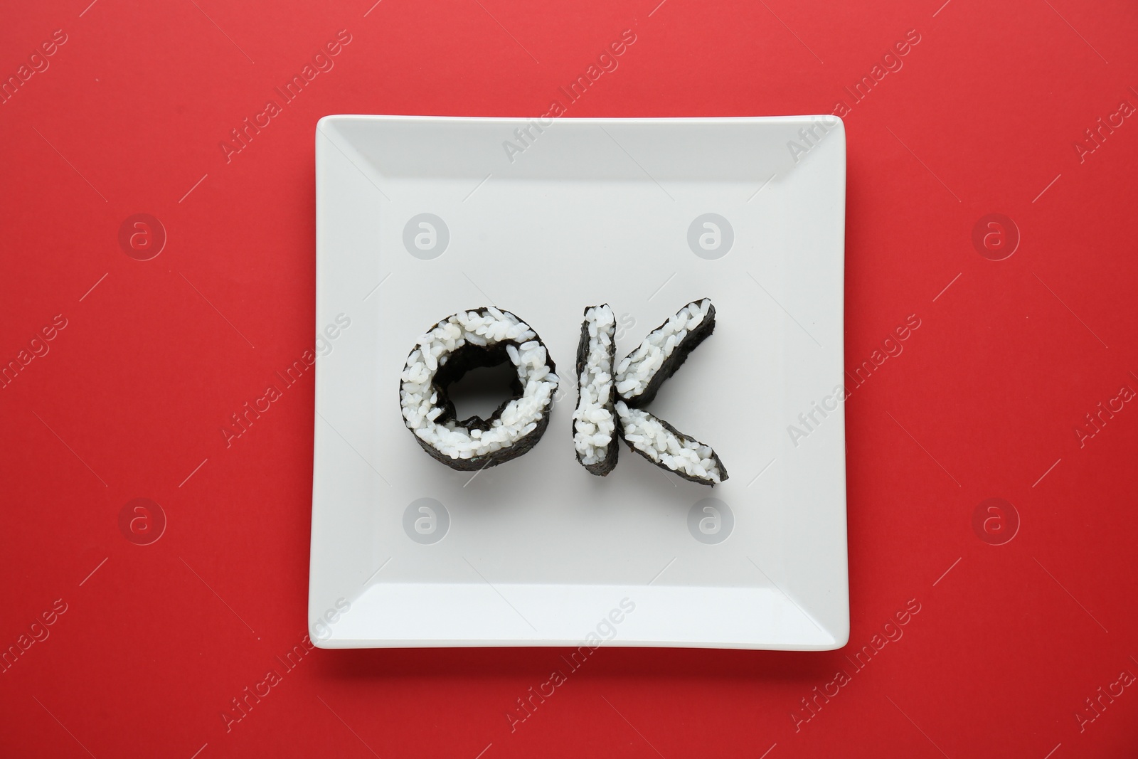 Photo of Word Ok made of sushi rolls on red background, top view
