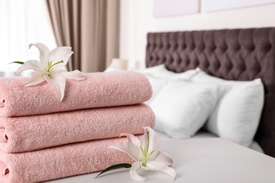 Photo of Stack of fresh towels with flowers on table in bedroom. Space for text