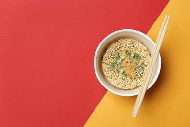 Cup of instant noodles with chopsticks on color background, top view. Space for text