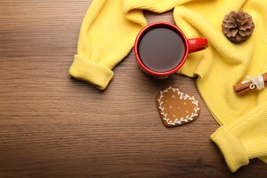 Photo of Cup of hot drink with yellow sweater and cookie on wooden table, flat lay. Space for text