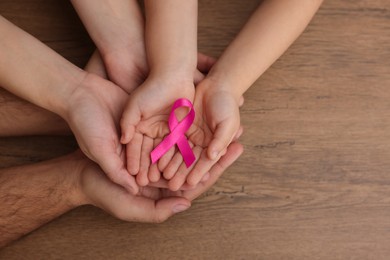 Photo of Family holding pink ribbon on wooden background, top view with space for text. Breast cancer awareness