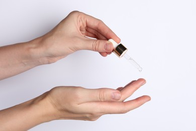 Photo of Woman applying cosmetic serum onto fingers on white background, closeup