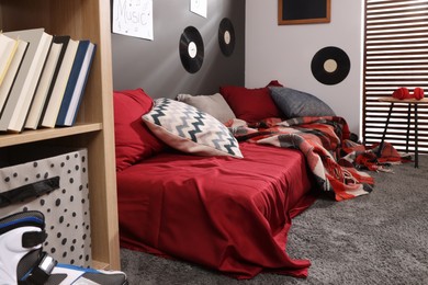 Wooden rack with books, bed and vinyl records on wall in teenager's room