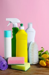 Spring cleaning. Detergents, tools and flowers on wooden table against pink background