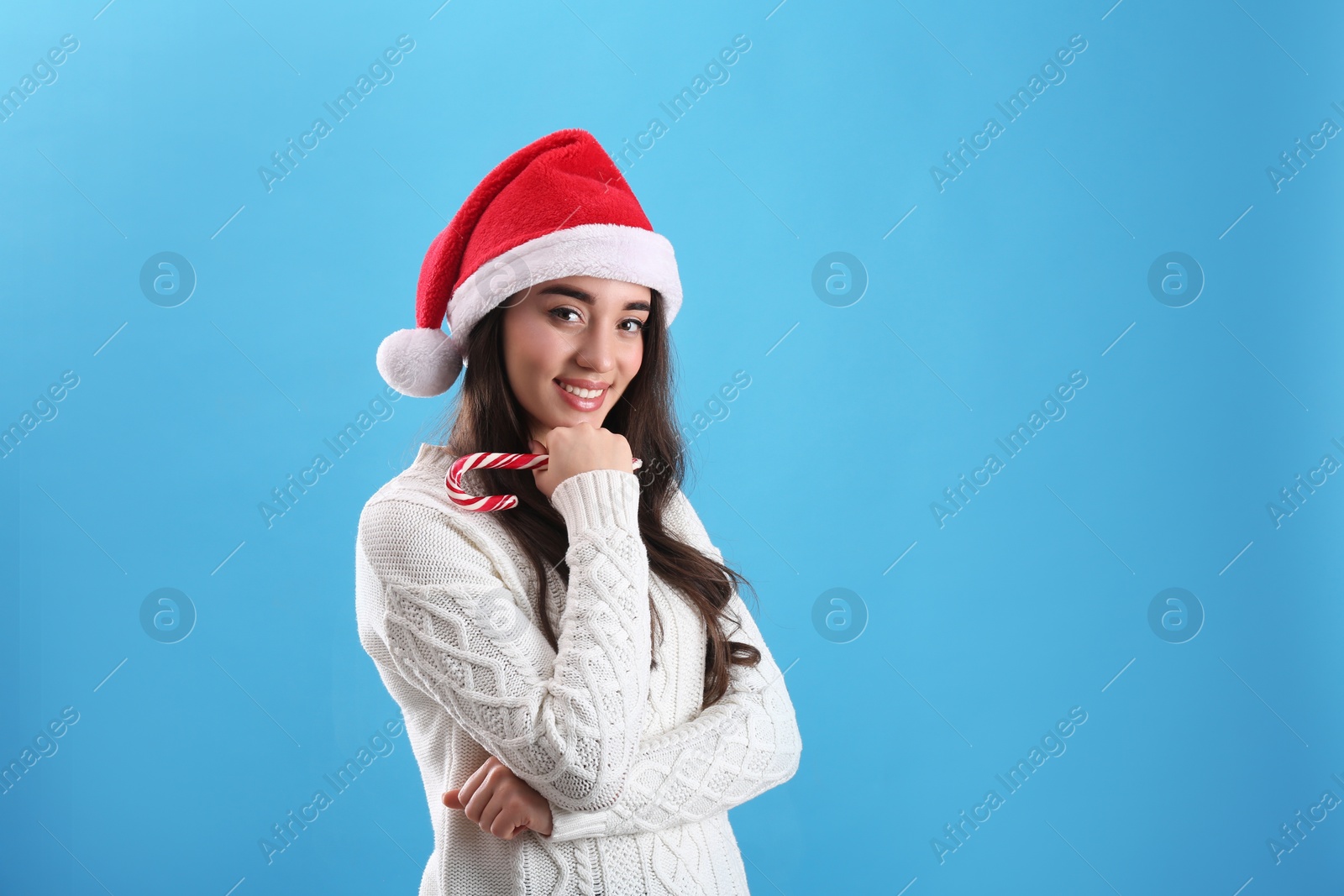 Photo of Beautiful woman in Santa Claus hat holding candy cane on light blue background