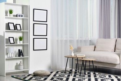 Photo of Stylish room interior with empty frames hanging on white wall near shelving unit