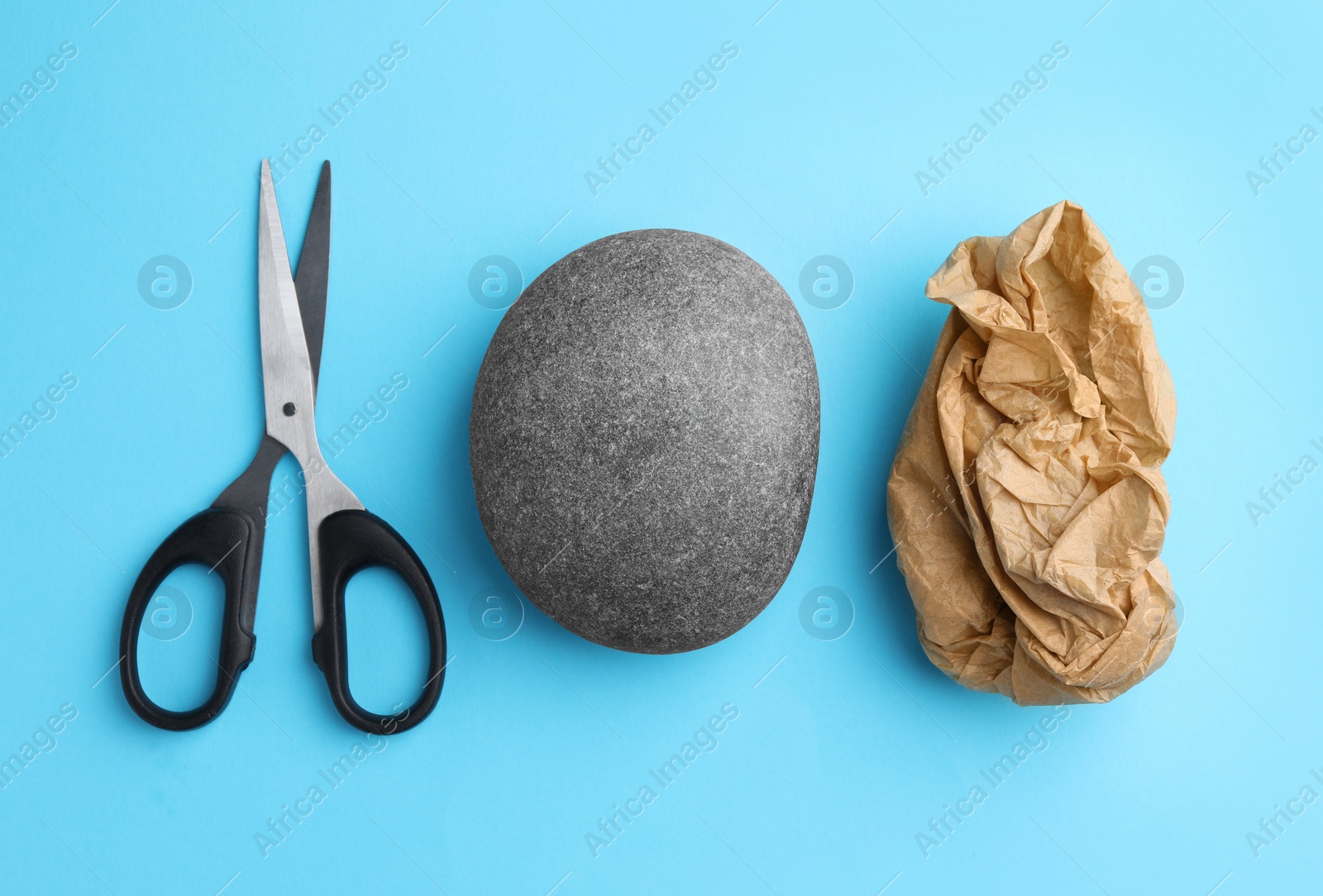 Photo of Rock, crumpled paper and scissors on light blue background, flat lay