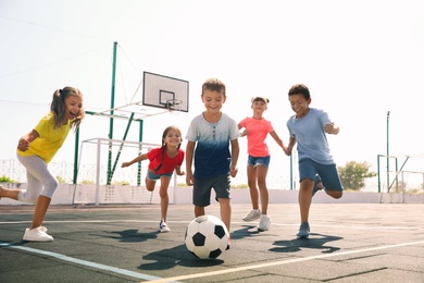 Photo of Cute children playing soccer outdoors on sunny day. Summer camp