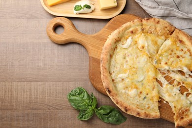 Photo of Delicious cut cheese pizza, basil and different kinds of cheese on wooden table, flat lay. Space for text