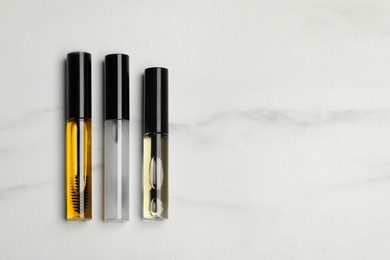 Photo of Tube of different eyelash oils on white marble table, flat lay. Space for text