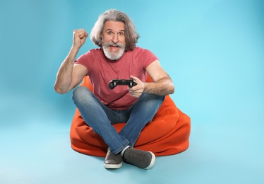 Photo of Emotional mature man playing video games with controller on color background