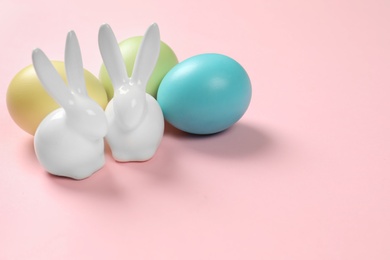 Photo of Ceramic Easter bunnies and dyed eggs on color background, space for text