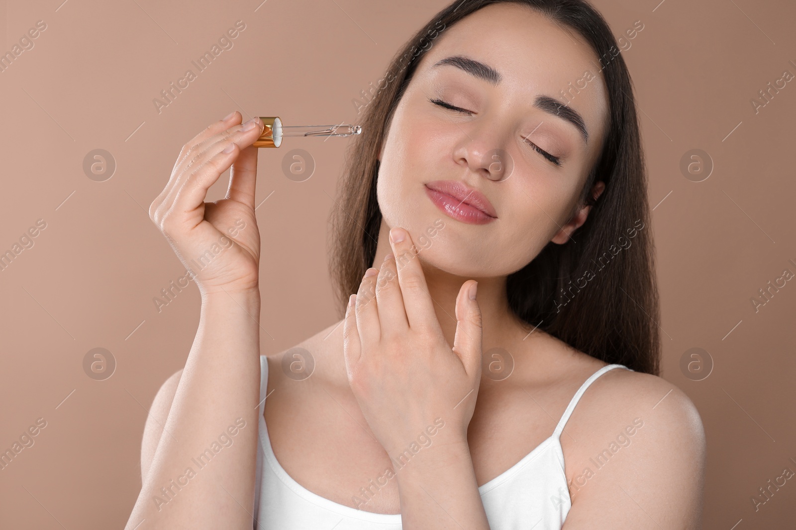 Photo of Beautiful woman applying essential oil onto face on brown background