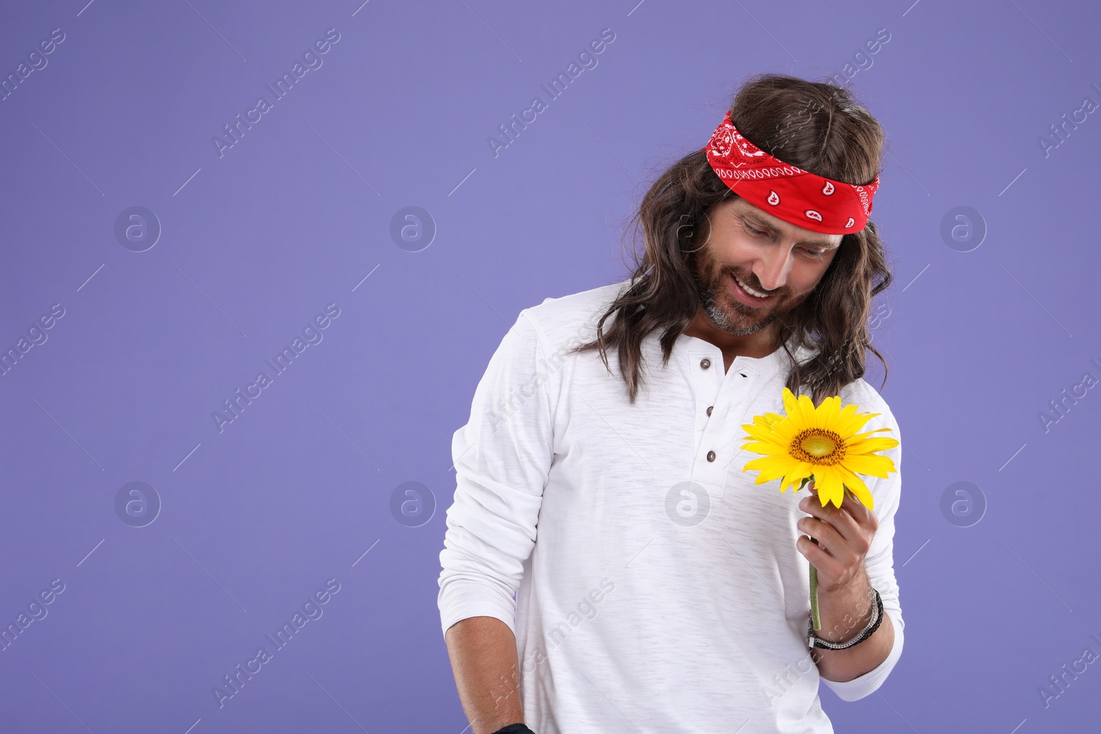 Photo of Stylish hippie man with sunflower on violet background, space for text