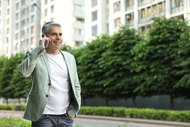 Photo of Handsome mature man talking on phone in city center. Space for text