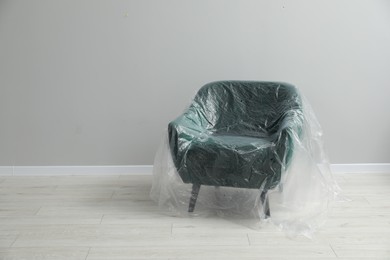 Stylish armchair covered with plastic film near light grey wall indoors. Space for text