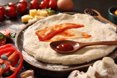 Photo of Pizza dough with tomato sauce and products on dark table, closeup